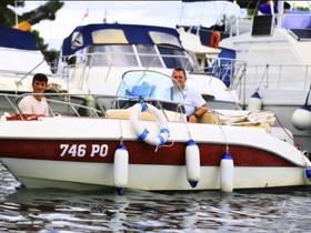 Two men enjoy a leisurely moment aboard a boat in a marina, surrounded by other vessels — a perfect snapshot of boating life.