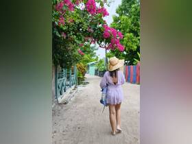 A woman walks down a picturesque path lined with vibrant flowers and greenery, creating a serene atmosphere perfect for leisurely strolls.
