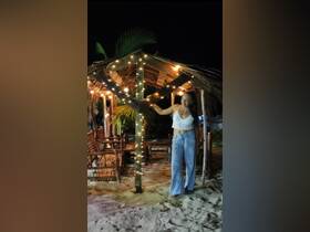 A woman poses under a beautifully lit beach hut at night, creating a perfect atmosphere for memorable moments by the shore.