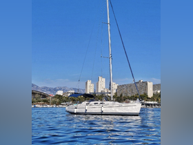 A picturesque sailboat glides through calm waters, showcasing its elegant design against a backdrop of urban architecture and mountains.