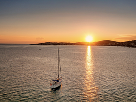 A serene sunset view featuring a sailboat anchored in calm waters, creating a picturesque scene perfect for tranquil evening cruises.