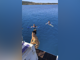 A joyful group enjoys swimming in crystal-clear waters, showcasing the perfect summer day on the water with friends.