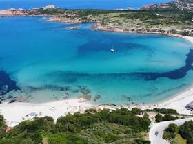 A stunning aerial view of a tranquil beach and coastline, showcasing crystal-clear turquoise waters and a serene sailing boat anchored nearby — perfect for island hopping adventures.