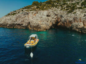 A vibrant boat anchored near a rocky coastline, with swimmers enjoying the clear waters — a perfect spot for adventure and exploration.