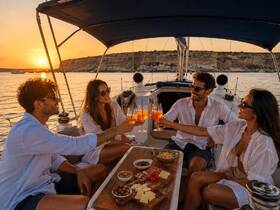 A group of friends toasting with cocktails on a yacht at sunset, enjoying a delightful evening with scenic views and delicious snacks.