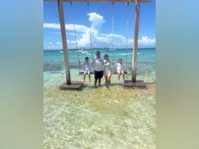 A joyful family enjoys a sunny day at the beach, swinging over the clear waters — a perfect moment of fun and relaxation in a tropical paradise.
