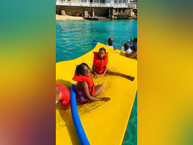 Two children enjoy a fun day on a floating mat in crystal-clear waters, wearing life jackets for safety — a perfect summer activity for families.