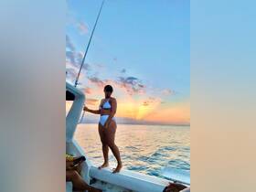 A woman poses on the deck of a boat against a stunning sunset backdrop, capturing the essence of a perfect evening on the water.