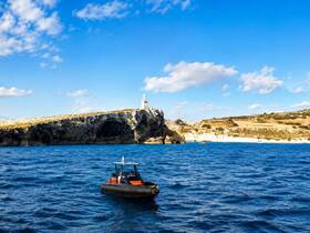 A sleek boat navigates the vibrant waters near a stunning coastal cliff, featuring a lighthouse in the background — a picturesque scene perfect for exploring scenic destinations.