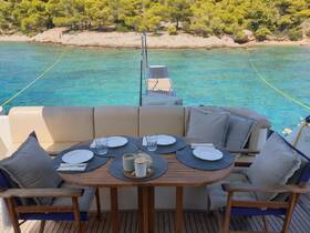 A beautifully arranged dining area on a boat, featuring a round table set with plates and glasses, perfect for enjoying meals while surrounded by stunning turquoise waters.