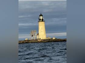 A distant view of a lighthouse standing on rocky terrain, surrounded by water under a cloudy sky.