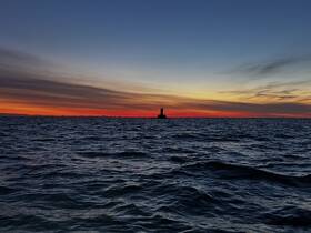 A stunning sunset over the ocean with a lighthouse silhouette, creating a picturesque scene perfect for evening boat trips.