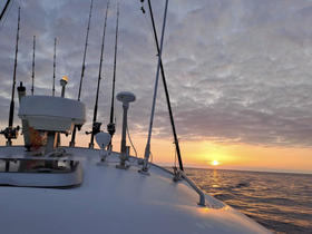 A serene sunset view from the bow of a fishing boat, showcasing fishing rods and the tranquil ocean — perfect for evening fishing adventures.