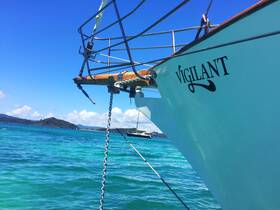 A stunning view of the bow of the 'Vigilant' boat against a backdrop of clear turquoise waters and a distant island, perfect for showcasing the beauty of sailing adventures.