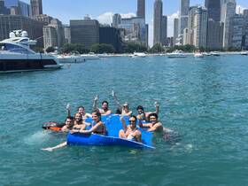 A lively group enjoys a fun day on a floating mat in the water, surrounded by the stunning Chicago skyline — perfect for summer parties and celebrations.