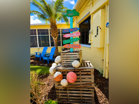 A colorful signpost in Key West points to popular local destinations, surrounded by tropical landscaping and wooden pallets.