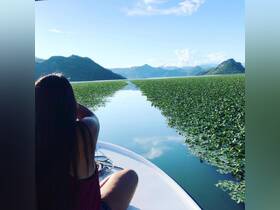 A serene view of a woman enjoying the picturesque landscape from a boat, surrounded by lush greenery and mountains — a perfect escape into nature.