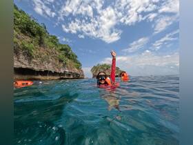A joyful snorkeler waves while exploring the vibrant waters near a scenic island, showcasing the excitement of underwater adventures.