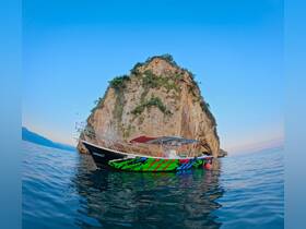 A vibrant boat named 'Legacy' anchored near a rocky cliff, showcasing a stunning backdrop of clear waters and a serene sky — perfect for exploring coastal landscapes.
