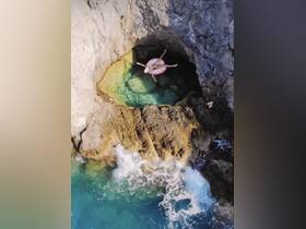 An aerial view of a person floating in a rocky cove, surrounded by crystal-clear waters — a perfect spot for relaxation and adventure in nature.