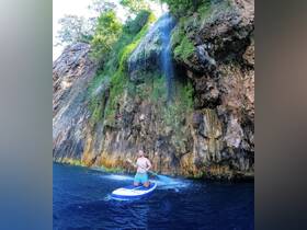 A paddleboarder enjoys an adventurous moment near a stunning waterfall, showcasing the beauty of outdoor water activities and scenic landscapes.