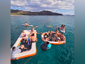 A lively group enjoys a fun day on the water with floating mats and swimming, perfect for a memorable party experience under the sun.