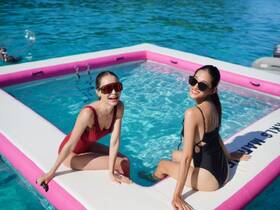Two friends enjoy a sunny day in a floating pool, showcasing fun and relaxation on the water — perfect for summer adventures.