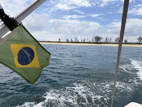 A scenic view from a boat featuring the Brazilian flag, with a beautiful coastline and clear waters in the background — perfect for exploring tropical destinations.