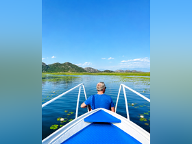A serene view of a man enjoying a peaceful boat ride on a picturesque lake, surrounded by lush mountains and blooming water lilies — perfect for nature lovers and tranquil escapes.