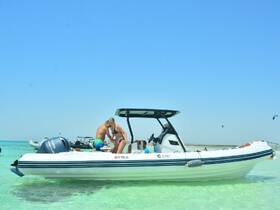 A couple enjoys their time on a boat in shallow waters, with kitesurfers visible in the background — a perfect scene for water sports enthusiasts.