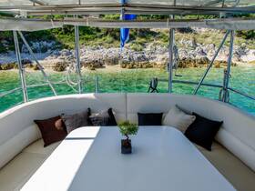 A cozy lounge area inside a boat featuring comfortable seating and a table, perfect for relaxing while enjoying views of the serene turquoise waters and rocky shoreline.