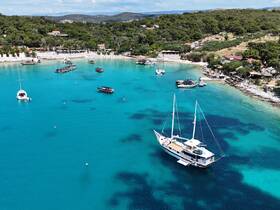 A stunning aerial view of a sailboat anchored in crystal-clear turquoise waters, surrounded by a picturesque bay and lush greenery, perfect for exploring coastal destinations.