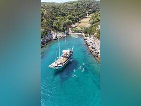 A group of swimmers enjoy the crystal-clear waters near a beautiful sailing boat anchored in a secluded cove, perfect for summer adventures.
