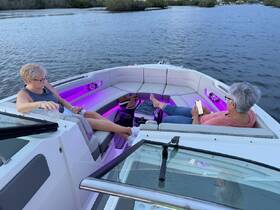 Two women relax in the stylish interior of a boat, enjoying the ambiance with colorful lighting — perfect for a cozy day on the water.