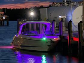 A sleek speedboat illuminated with colorful lights is docked at a marina, creating a vibrant scene against the twilight sky.