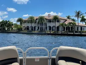 A scenic view from a pontoon boat showcasing a beautiful waterfront mansion surrounded by palm trees, perfect for a relaxing day on the water.