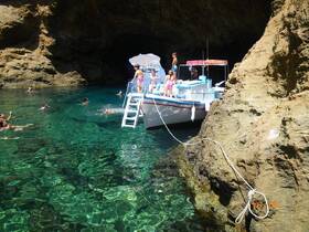 A lively scene at a cove where children and adults enjoy swimming around a boat, creating a perfect summer day on the water.