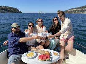 A joyful group toasts with cocktails aboard a boat, enjoying snacks like watermelon and chips — a perfect scene for a fun day on the water.