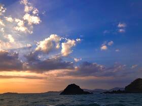 A stunning sunset over the coastline, with dramatic clouds reflecting the warm hues of the evening sky — a perfect backdrop for a serene boating experience.