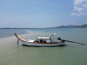 A traditional fishing boat anchored in shallow waters, with people enjoying the serene beach environment in the background.
