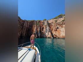 A man stands on the bow of a boat, admiring stunning cliffs and crystal-clear waters — a perfect moment for exploration and adventure.
