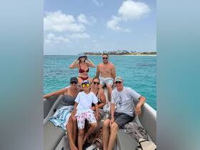 A cheerful family enjoys a day on the water, posing together on a boat with stunning turquoise waters in the background — perfect for memorable summer adventures.
