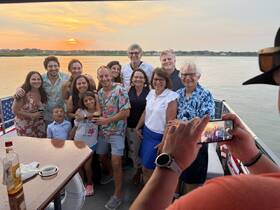 A joyful group of family and friends gathers for a sunset photo on a boat, celebrating together against a picturesque backdrop — perfect for memorable gatherings and special occasions.