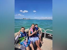 Three kids enjoy a sunny day on a boat, smiling and sharing snacks — a perfect moment of fun and adventure on the water.