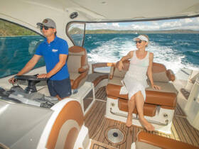 A stylish interior view of a boat's helm with a captain at the wheel and a guest relaxing on the seating area, showcasing the comfort and elegance of onboard spaces.