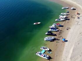 A vibrant beach scene with multiple boats anchored and groups of people enjoying the sun and water activities — perfect for a fun day out on the water.