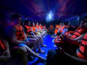 A group of guests wearing life jackets sits inside a boat cabin, ready for an adventure on the water. The cozy interior provides a safe and comfortable environment for passengers.
