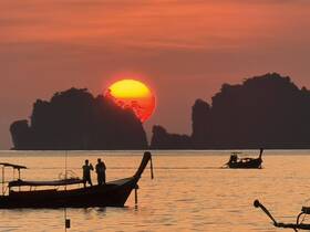 A couple enjoys a romantic moment on a boat at sunset, with stunning silhouettes of islands in the background — a perfect scene for memorable experiences on the water.