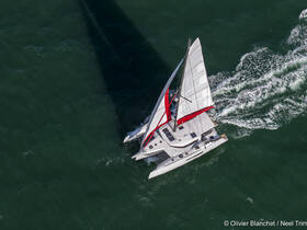 Aerial view of a sleek catamaran sailing through vibrant waters, showcasing its elegant design and performance on the open sea.