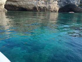 A stunning view of a coastal cave with crystal-clear waters, showcasing a group enjoying the serene beauty of the destination.